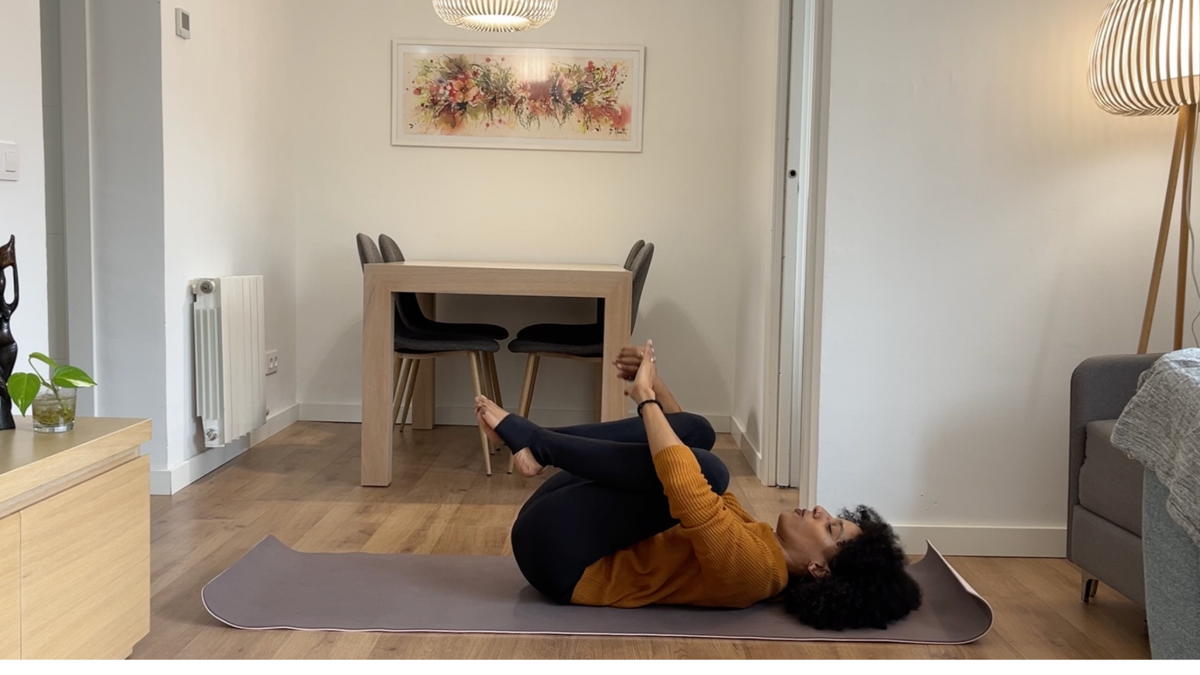 Laia Bové lying on her back and hugging both knees in toward her chest with hands around her shins.